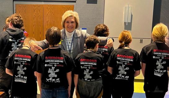 Students wearing black shirts for robotics competition that say sponsored by Carolina Handling on the back.
